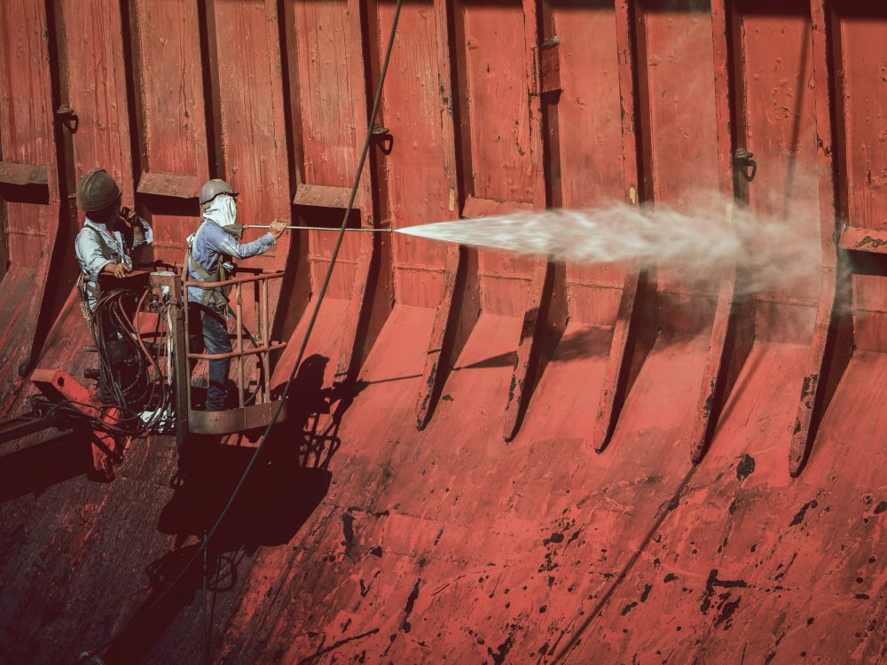 Washing and Cleaning, Close up arms of man holding high pressure water gun cleaning with Cargo ship under repair in floating dry dock in  shipyard Thailand.